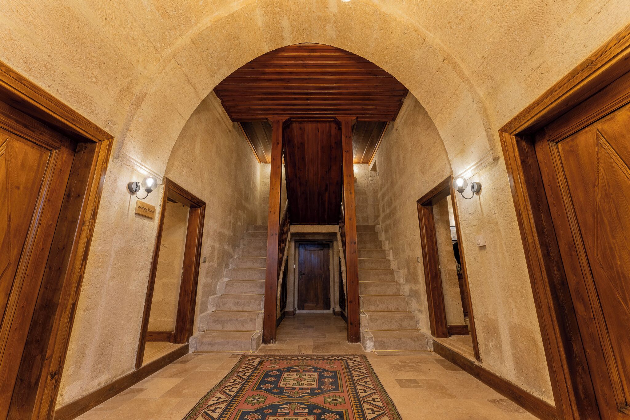 Un couloir avec un escalier en bois, des murs en pierre et une moquette à motifs.