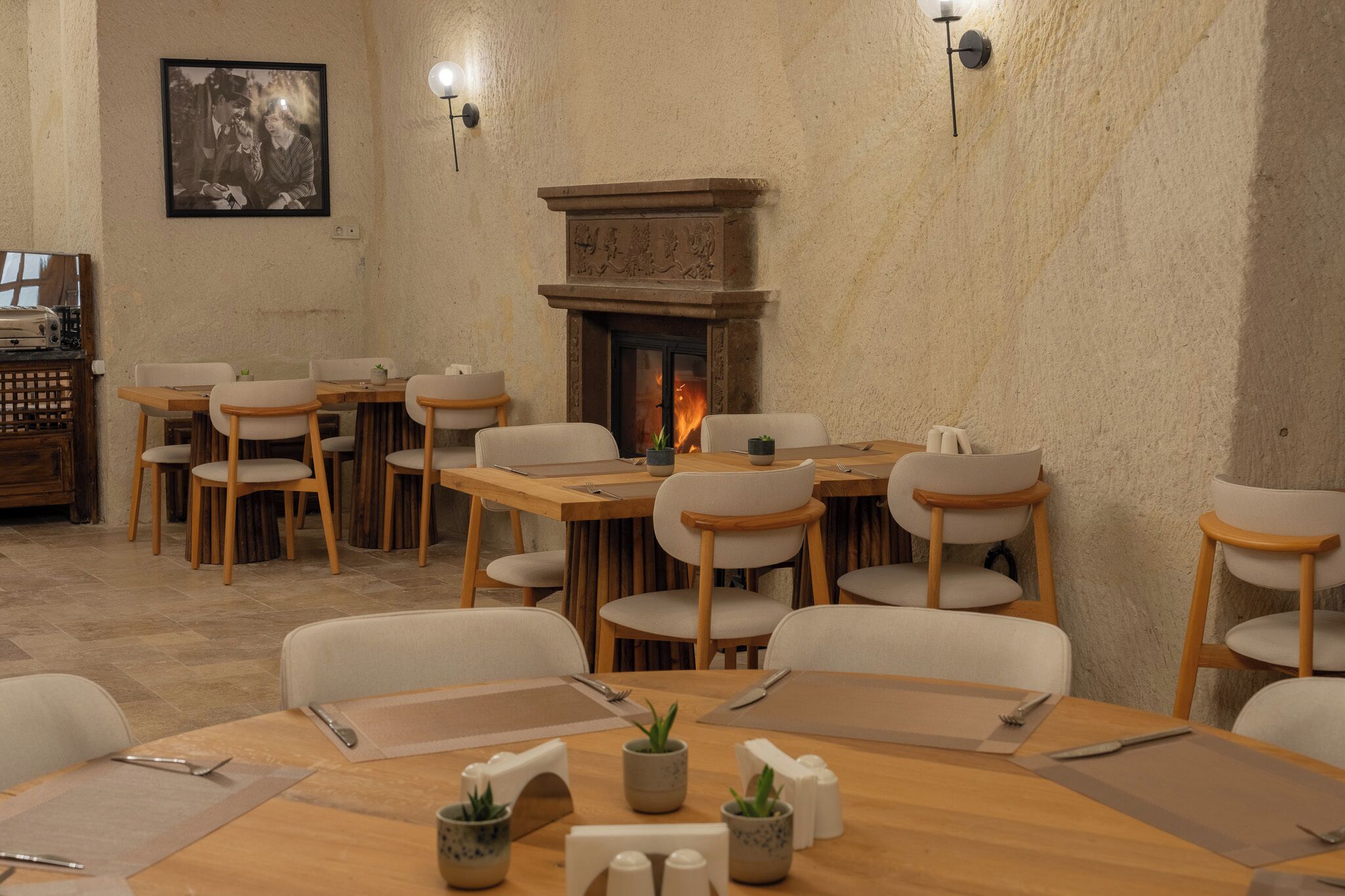 A dining area with wooden tables and chairs, a fireplace, and a framed picture on the wall.