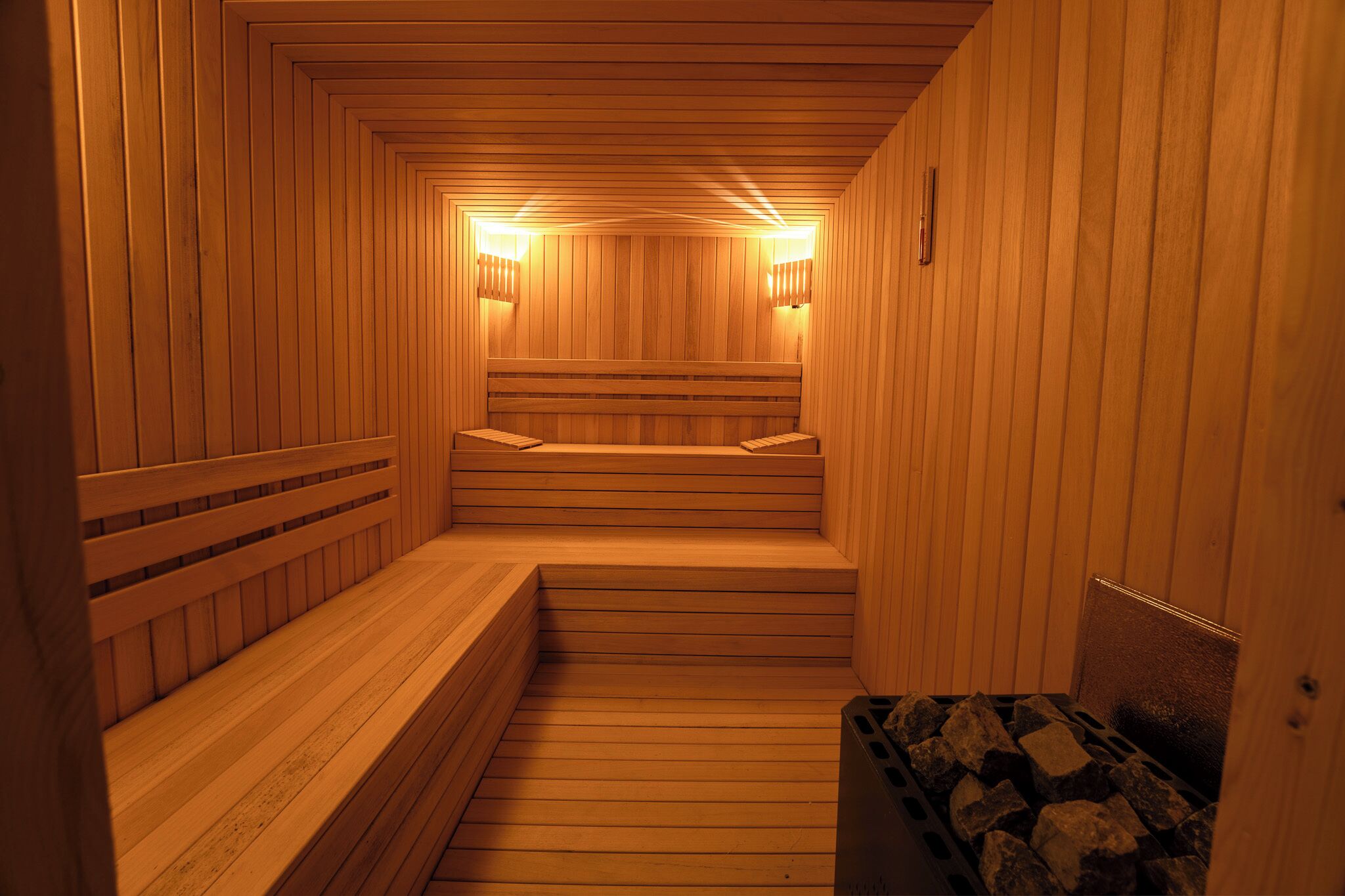 A sauna with wooden benches and walls, a bench at the end, and a trash bin with rocks.