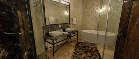Une salle de bain avec une douche à parois de verre, un grand miroir, deux lavabos, une baignoire et une porte en bois.