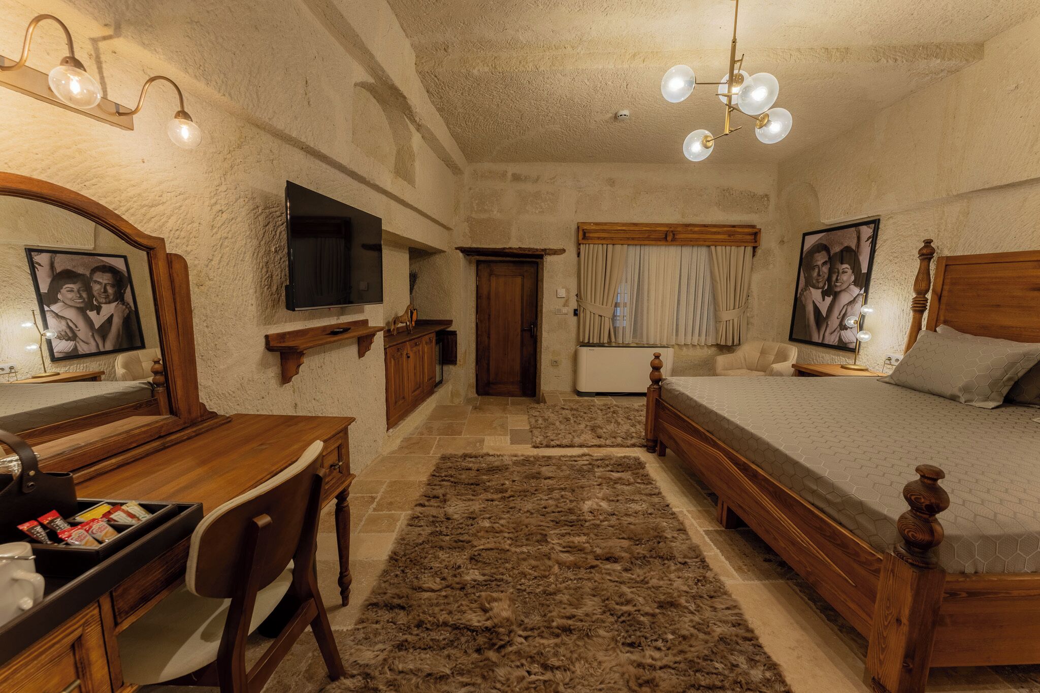 A bedroom with a wooden bed, a desk with a chair, a television, and a large mirror.