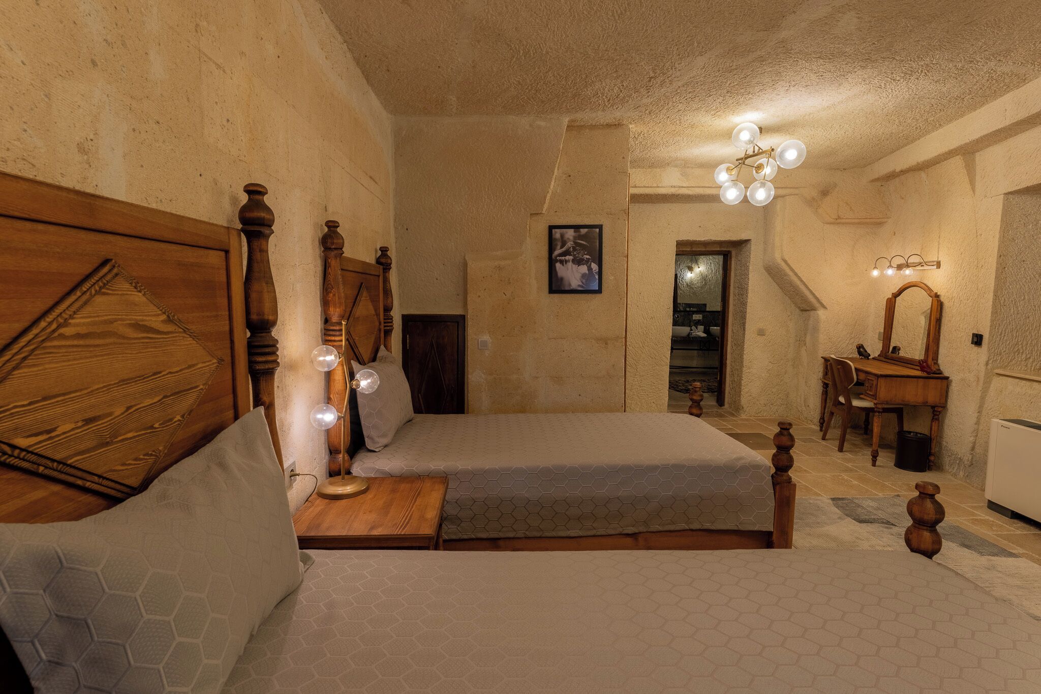 A bedroom with two beds, wooden headboards, a bedside table with a lamp, a mirror, and a framed picture on the wall.