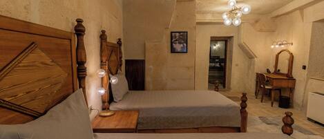 A bedroom with two beds, wooden headboards, a bedside table with a lamp, a mirror, and a framed picture on the wall.