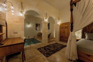 Un dormitorio con cama con dosel, un escritorio de madera, una silla, una piscina pequeña y una pared de piedra con arcos.