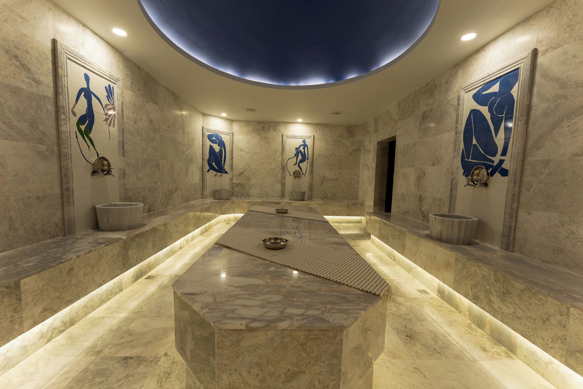 A modern spa room with a central heated stone slab, marble walls, and abstract wall art.
