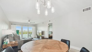 Ein moderner Essbereich mit einem runden Holztisch und schwarzen Stühlen, einem Deckenventilator und Blick ins Freie durch große Fenster.