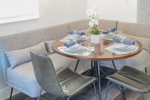 Ein runder Esstisch mit vier Stühlen, eine Vase mit weißen Blumen und ordentlich gefaltete blaue Servietten.