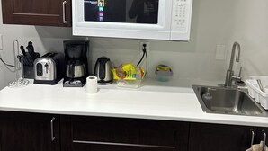 A kitchen with dark wooden cabinets, a white countertop, a microwave, a toaster, a coffee maker, and a sink. - The Last Resort with private entrance. In Basement. (Winnipeg)