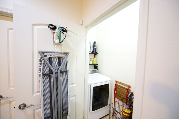 A laundry area with a washing machine, a drying rack, and a shelf with cleaning supplies.