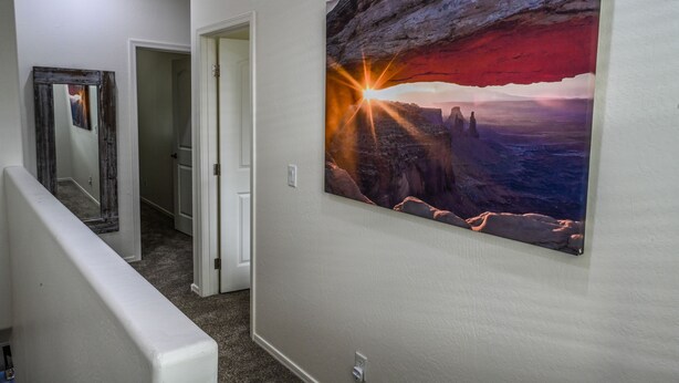 Un pasillo con un cuadro enmarcado de una puesta de sol sobre un cañón, una puerta y una pared blanca.