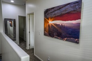 A hallway with a framed painting of a sunset over a canyon, a door, and a white wall.