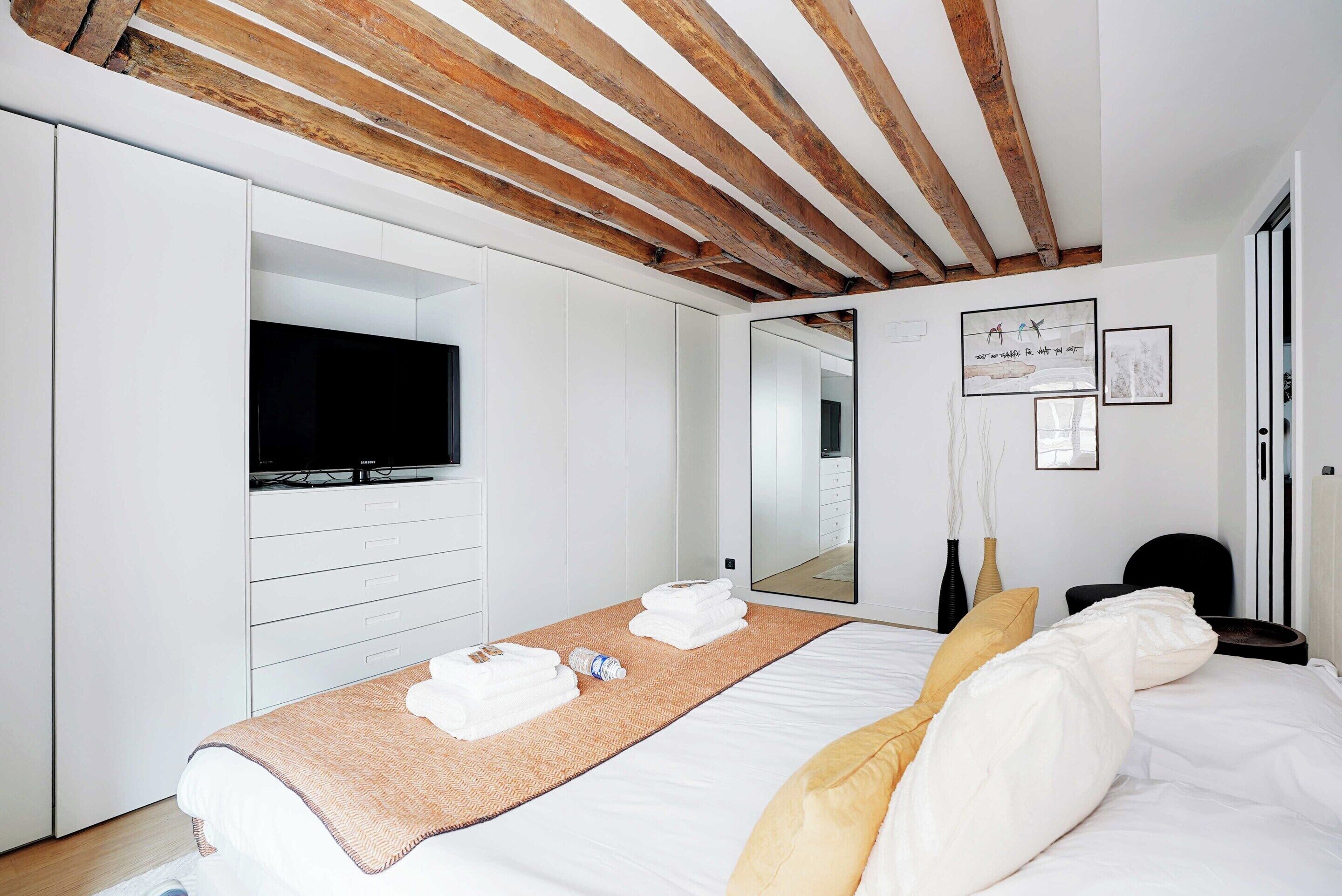 A modern hotel room with a large bed, a flat-screen TV, a wardrobe, and a mirror.