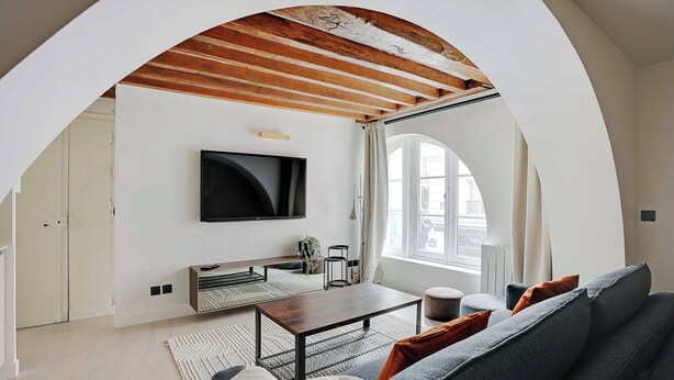 Ein modernes Wohnzimmer mit Flachbildfernseher, einer Couch, einem Couchtisch und einem großen Fenster, das für natürliches Licht sorgt.