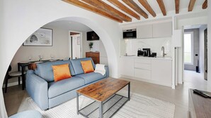 Ein modernes Wohnzimmer mit Sofa, Couchtisch und einem durch eine Rundbogenöffnung sichtbaren Küchenbereich.