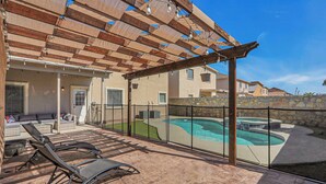 A covered outdoor area with a pool, lounge chairs, and a patio with a stone wall. - Huge Oasis Retreat>Arcade>Pool Table>Heated Pool & Spa>Super H on AirBB (El Paso)