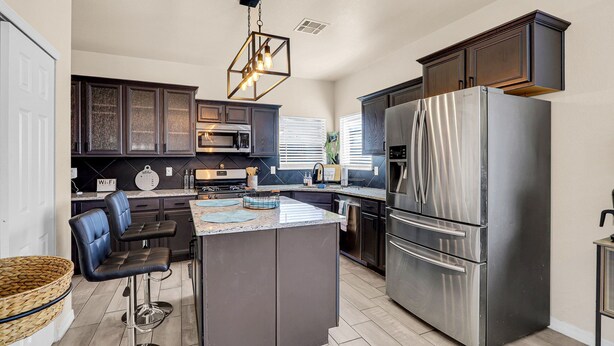 A modern kitchen with dark cabinetry, a stainless steel refrigerator, and a central island with bar stools. - Huge Oasis Retreat>Arcade>Pool Table>Heated Pool & Spa>Super H on AirBB (El Paso)