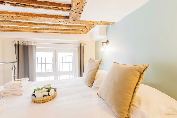 A hotel room with a bed, pillows, a basket of toiletries, and a view of the outside.