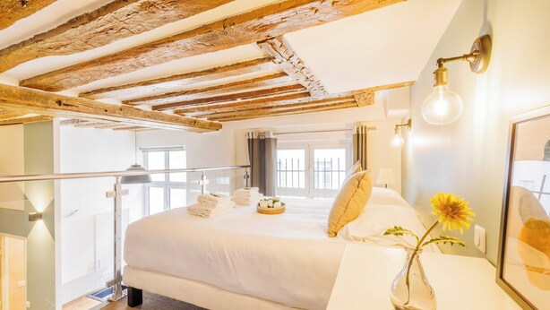 Ett hotellrum med en stor säng, ett litet bord med en vas med blommor och ett träpanelat tak.