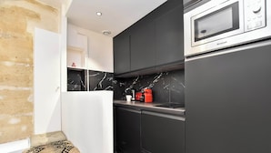 A modern kitchen with black cabinets, a marble backsplash, and a Brandt microwave. - Cozy Apartment - 1br/4p - Sentier (Paris)