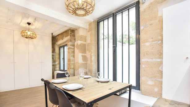 A dining area with a wooden table set for four, black chairs, and a large window with a view of greenery. - Cozy Apartment - 1br/4p - Sentier (Paris)