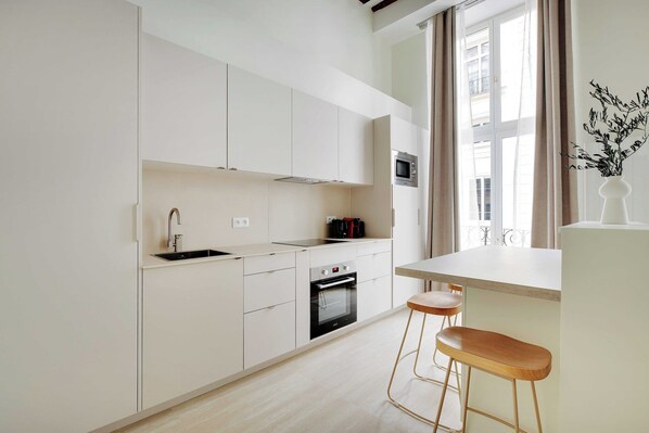 Eine moderne Küche mit weißen Schränken, einem Einbauofen, einer Mikrowelle und einem Fenster mit Vorhängen.