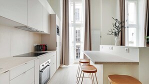 A modern kitchen with white cabinetry, a built-in oven, and a window with curtains. - Charming Apartment - 1br/5p - Quartier du Mail (Paris)