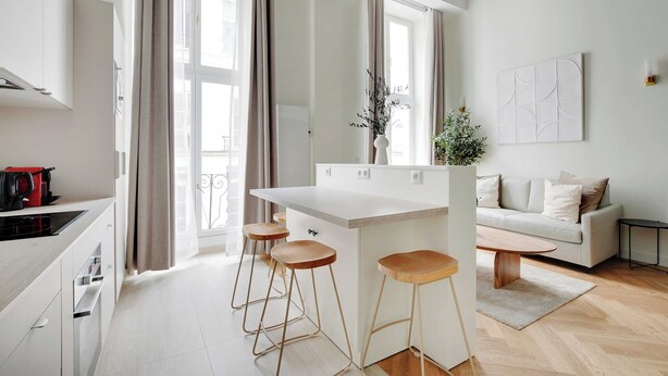 A modern kitchen with a white countertop, wooden stools, and a central island. - Charming Apartment - 1br/5p - Quartier du Mail (Paris)
