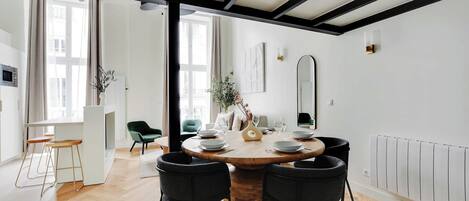 A dining area with a round wooden table, four black chairs, and a white radiator on the wall.