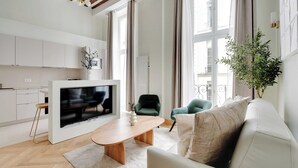 A modern living room with a flat-screen TV, a wooden coffee table, a sofa, and two green armchairs. - Charming Apartment - 1br/5p - Quartier du Mail (Paris)