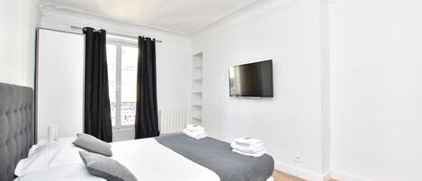 Un dormitorio moderno con una cama grande, un televisor de pantalla plana y un ventanal con cortinas.