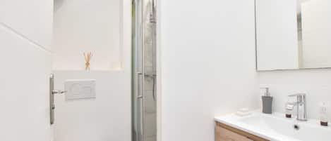 Un baño moderno con inodoro blanco, cabina de ducha de vidrio, tocador de madera con lavamanos y espejo.