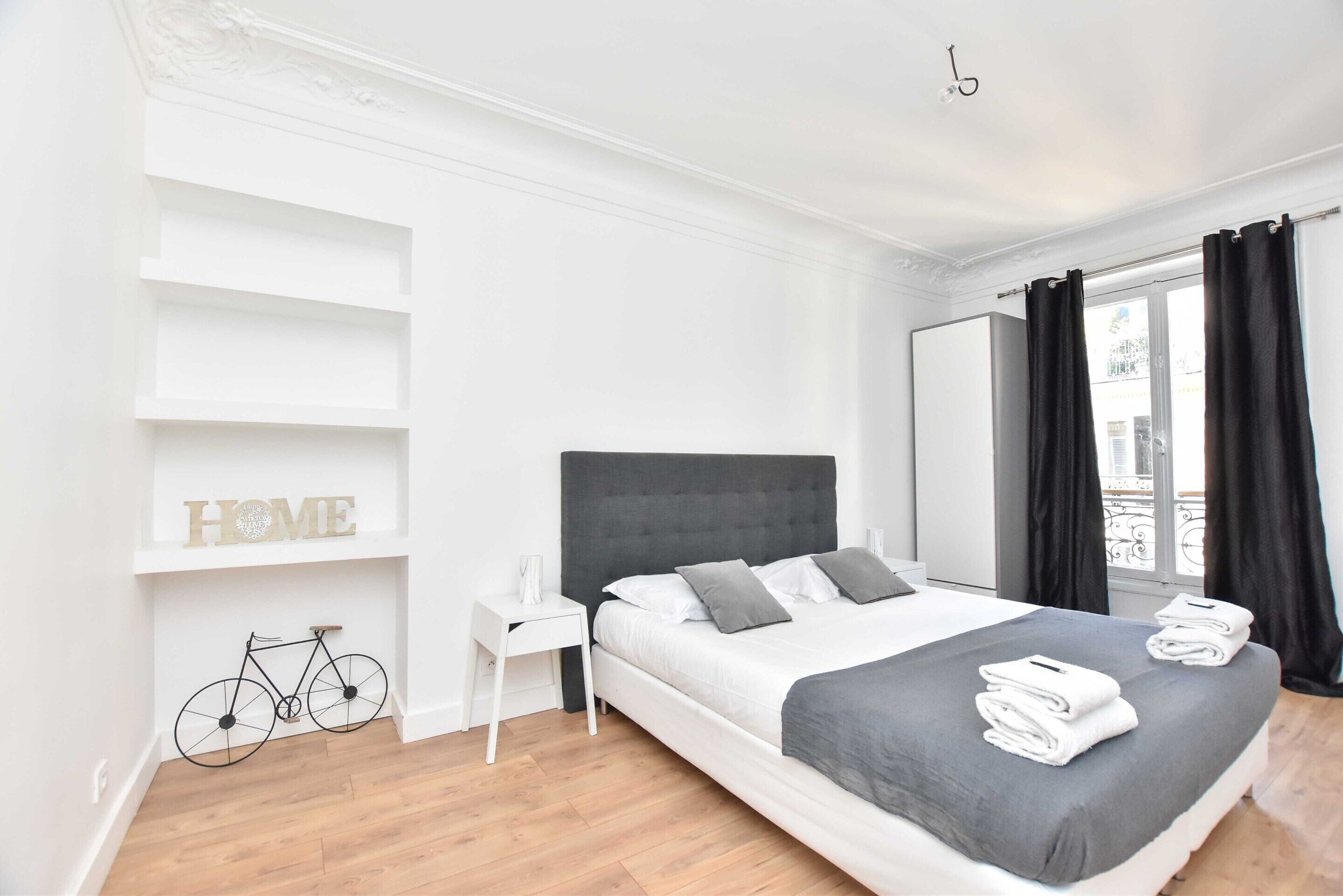 A modern bedroom with a large bed, a bicycle, and a 'HOME' sign on the wall.