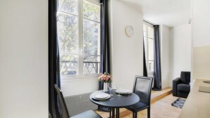 Un comedor moderno con una mesa redonda para dos personas, un florero con flores y vistas a la ciudad a través de amplias ventanas.