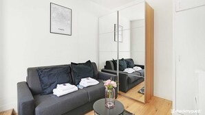 Una habitación moderna y minimalista con un sofá gris, una pequeña mesa redonda con un jarrón de flores y un mueble espejo grande.