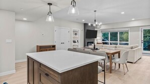 A modern kitchen with a central island, dining area with chairs, a sofa, and a TV. - 3 Bed/2 Bath Sparrowhawk Lodge-TopFloor-Creekside (Dead Man's Flats)