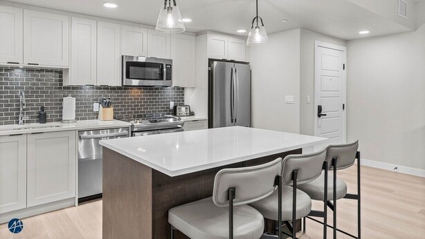 A modern kitchen with white cabinets, a central island with bar stools, stainless steel appliances, and pendant lighting. - 3 Bed/2 Bath Sparrowhawk Lodge-TopFloor-Creekside (Dead Man's Flats)