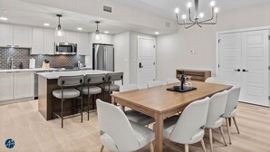 A modern kitchen with white cabinets, a central island with bar stools, a wooden dining table, and a chandelier. - 3 Bed/2 Bath Sparrowhawk Lodge-TopFloor-Creekside (Dead Man's Flats)