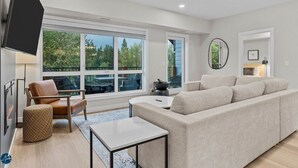 A modern living room with a large window, a sofa, a coffee table, and a TV mounted on the wall. - 3 Bed/2 Bath Sparrowhawk Lodge-TopFloor-Creekside (Dead Man's Flats)
