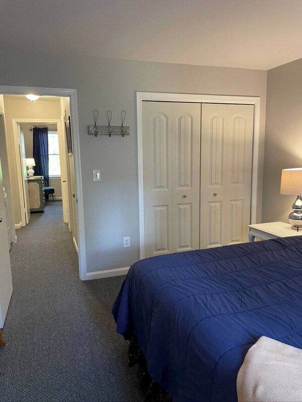 A bedroom with a large bed, a desk with a lamp, and a wardrobe.