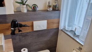 A modern bathroom with a toilet, a sink, a hairdryer, and a toilet paper holder. - Apartment kitchen, WLAN, SMART TV, modern, single bed (Roding)