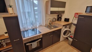 A compact kitchen with a built-in oven, a sink, a coffee maker, and a microwave. - Apartment kitchen, WLAN, SMART TV, modern, single bed (Roding)
