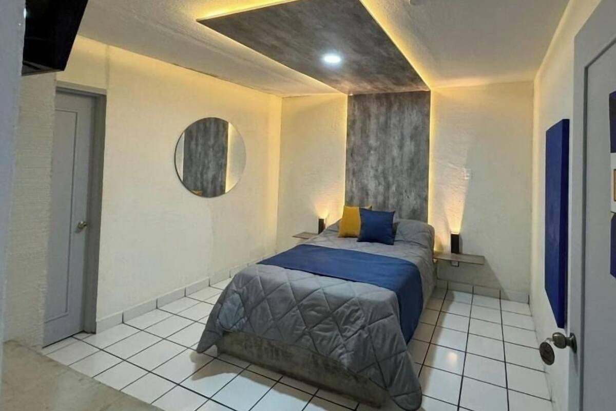 Un dormitorio con una cama, un espejo redondo y un televisor montado en la pared.