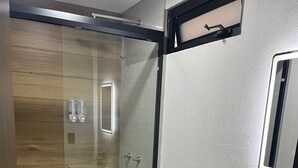 Ein modernes Badezimmer mit Duschkabine aus Glas, einer weißen Toilette, einem Waschbecken und einem Spiegel darüber.