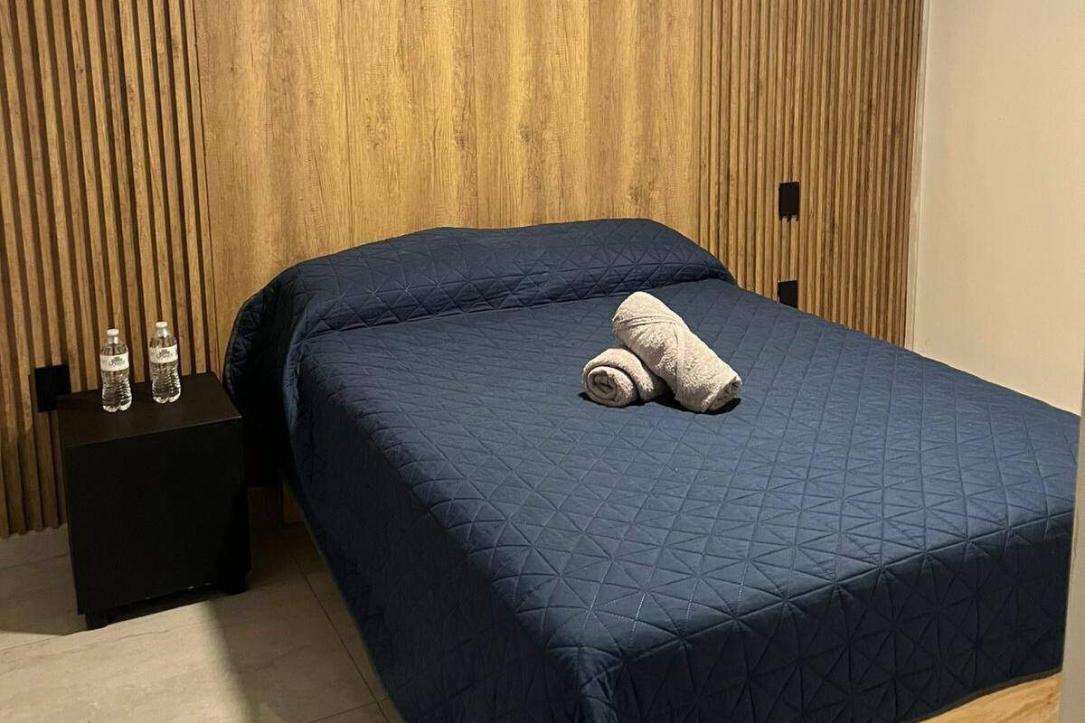 Un dormitorio con cama, mesita de noche, ventilador de techo y paneles de madera en la pared.