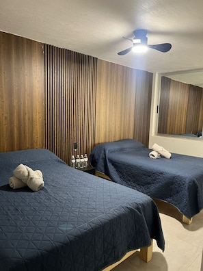 Ein Hotelzimmer mit zwei Betten, Holzvertäfelung, einem Deckenventilator und einem Fenster.