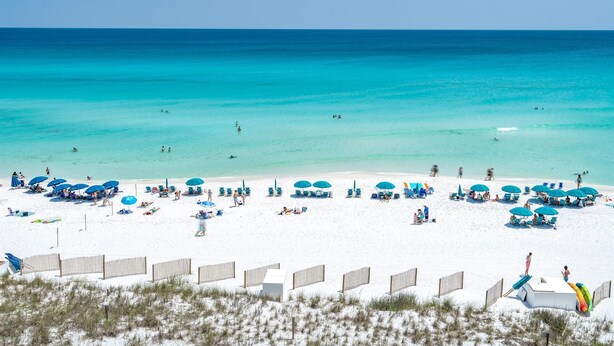 A beach with white sand, clear turquoise water, and blue umbrellas. - Emerald Dunes 501*Penthouse*Pool*Hot Tub*Gulf View (Destin)