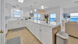 A modern kitchen with white cabinets, a large island, pendant lights, and a view of the ocean. - Emerald Dunes 501*Penthouse*Pool*Hot Tub*Gulf View (Destin)