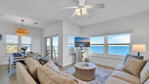 A spacious living room with a large sofa, a coffee table, and a television. There are large windows with a view of the ocean. - Emerald Dunes 501*Penthouse*Pool*Hot Tub*Gulf View (Destin)