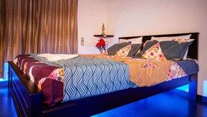 A bed with a patterned bedspread, a bedside table with a decorative item, and a curtain with a polka dot pattern. - Ravana Egyptians Villa (Chennai)
