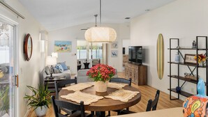 Un salon moderne avec un coin repas, comprenant une table ronde avec des sets de table, une grande plante en pot et un luminaire suspendu.